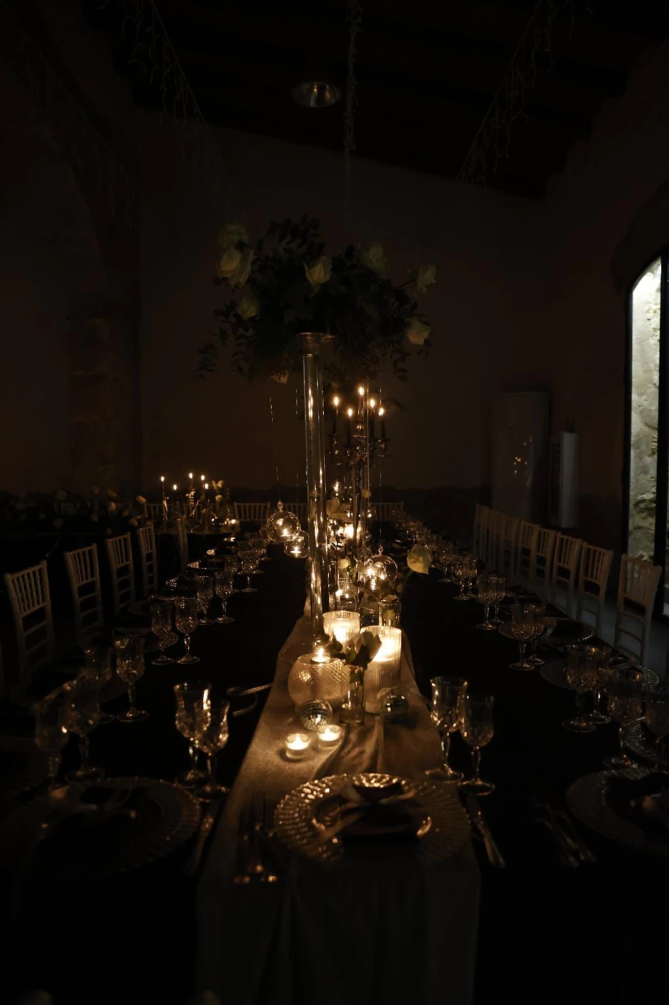 La tavolata vista per lungo, col centrotavola alto e i candelabri accesi